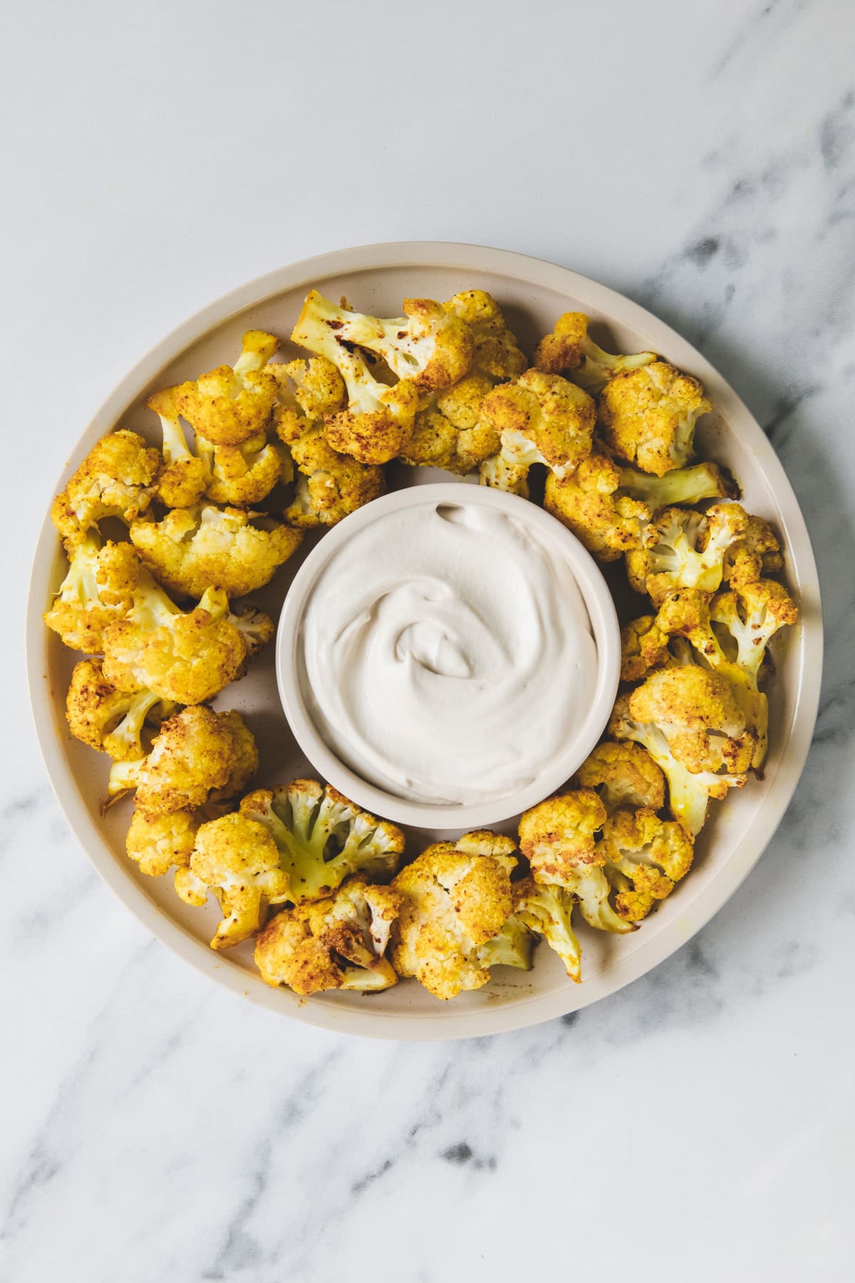 A platter of roasted cauliflower with dipping sauce in the centre.
