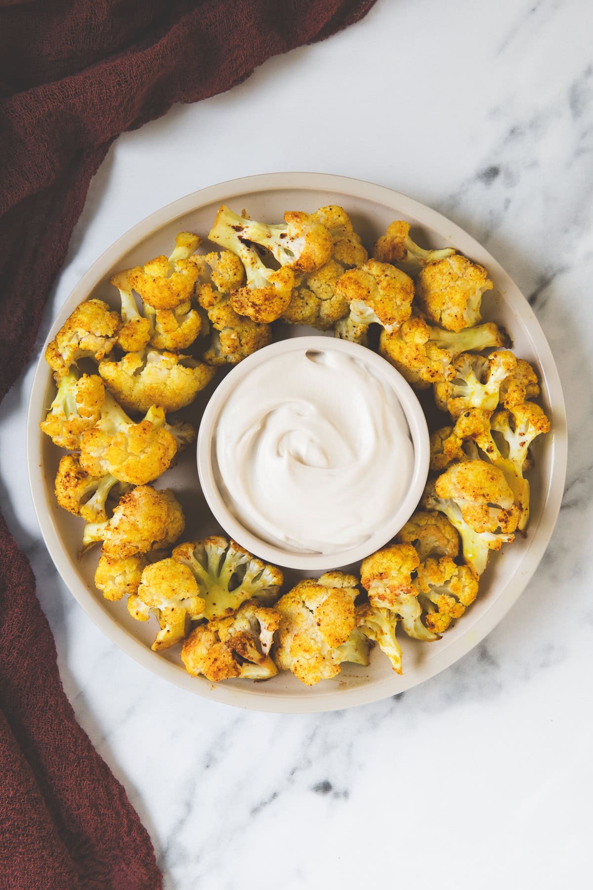 A ring of spicy cauliflower bites with a bowl of creamy garlic sauce in the centre.