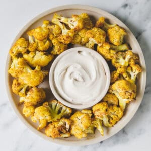 A platter of roasted cauliflower with dipping sauce in the centre.