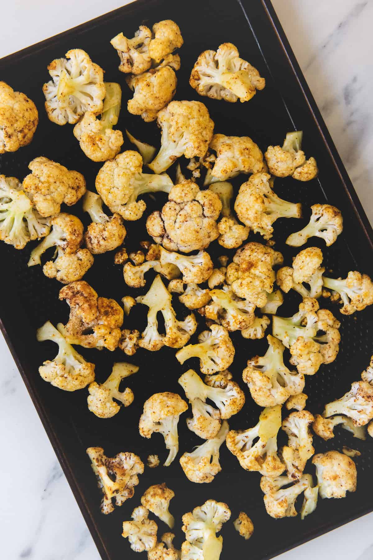 Seasoned cauliflower florets evenly spread on a baking sheet.