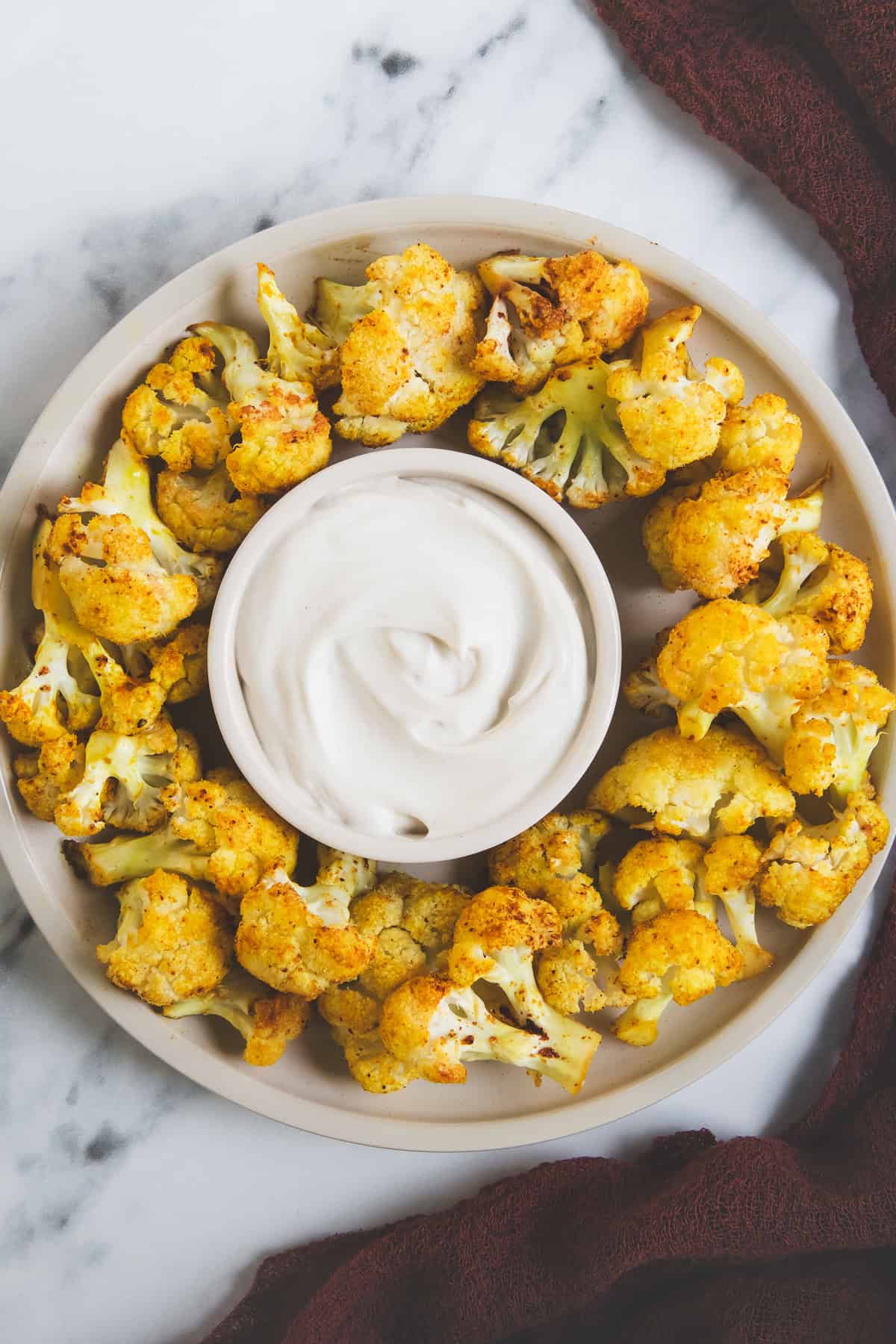 A platter of roasted cauliflower with dipping sauce in the centre.