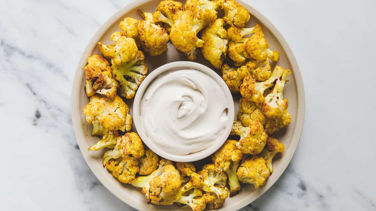 A plate of roasted buffalo cauliflower with a bowl of dipping sauce in the middle.
