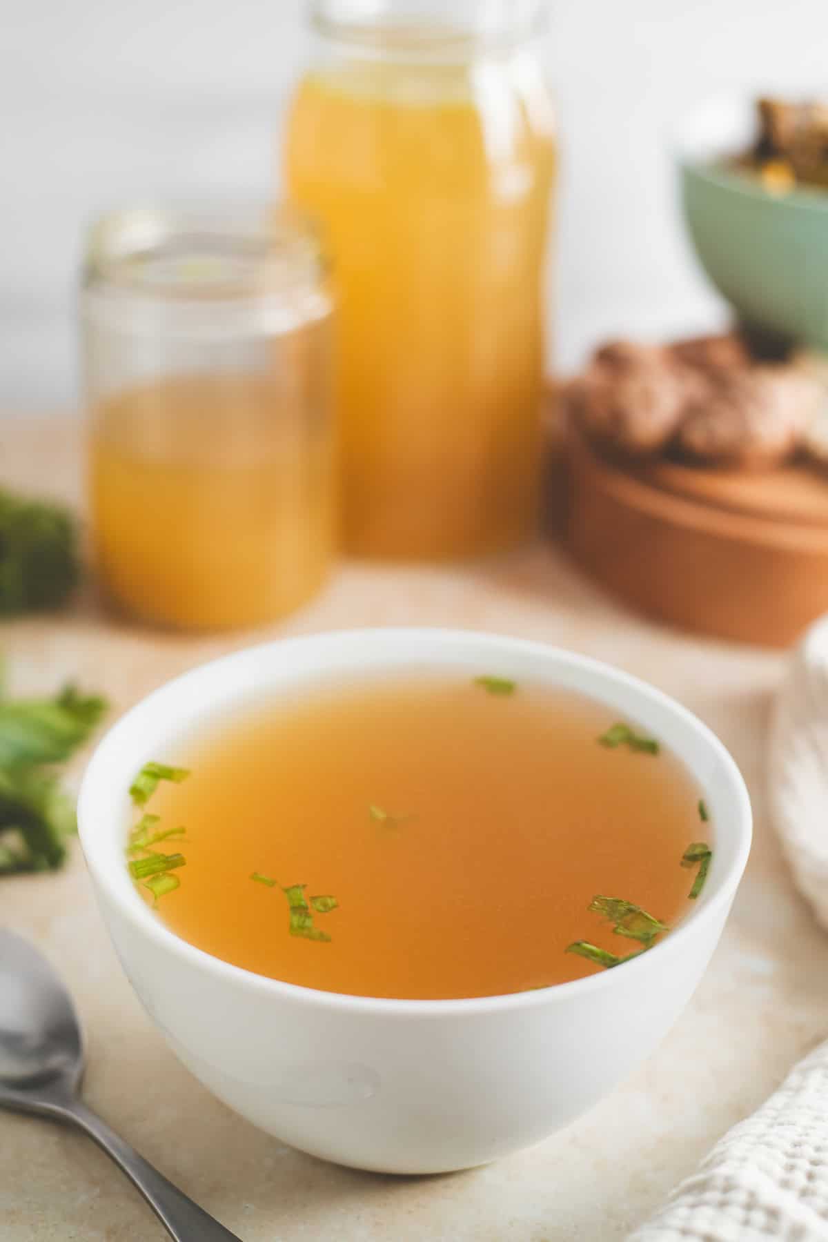 A bowl of clear, golden broth garnished with green onion.