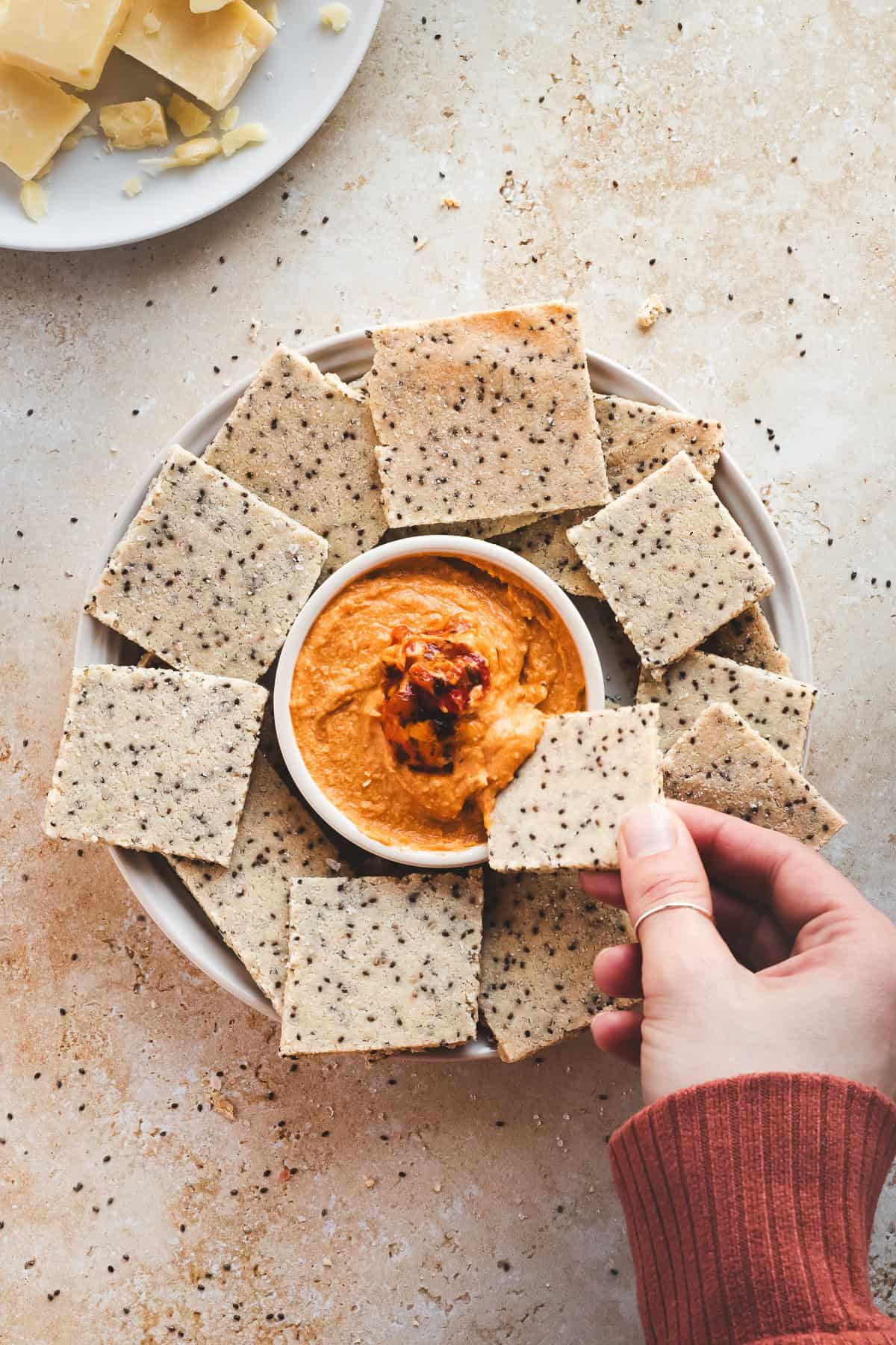 A chia seed cracker being dipped in red pepper hummus.