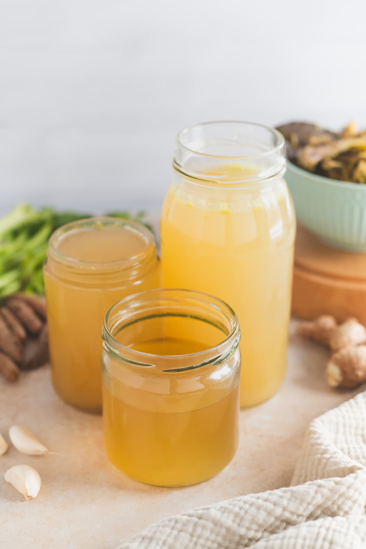 Fresh celery, ginger, turmeric and garlic with three jars of golden broth.