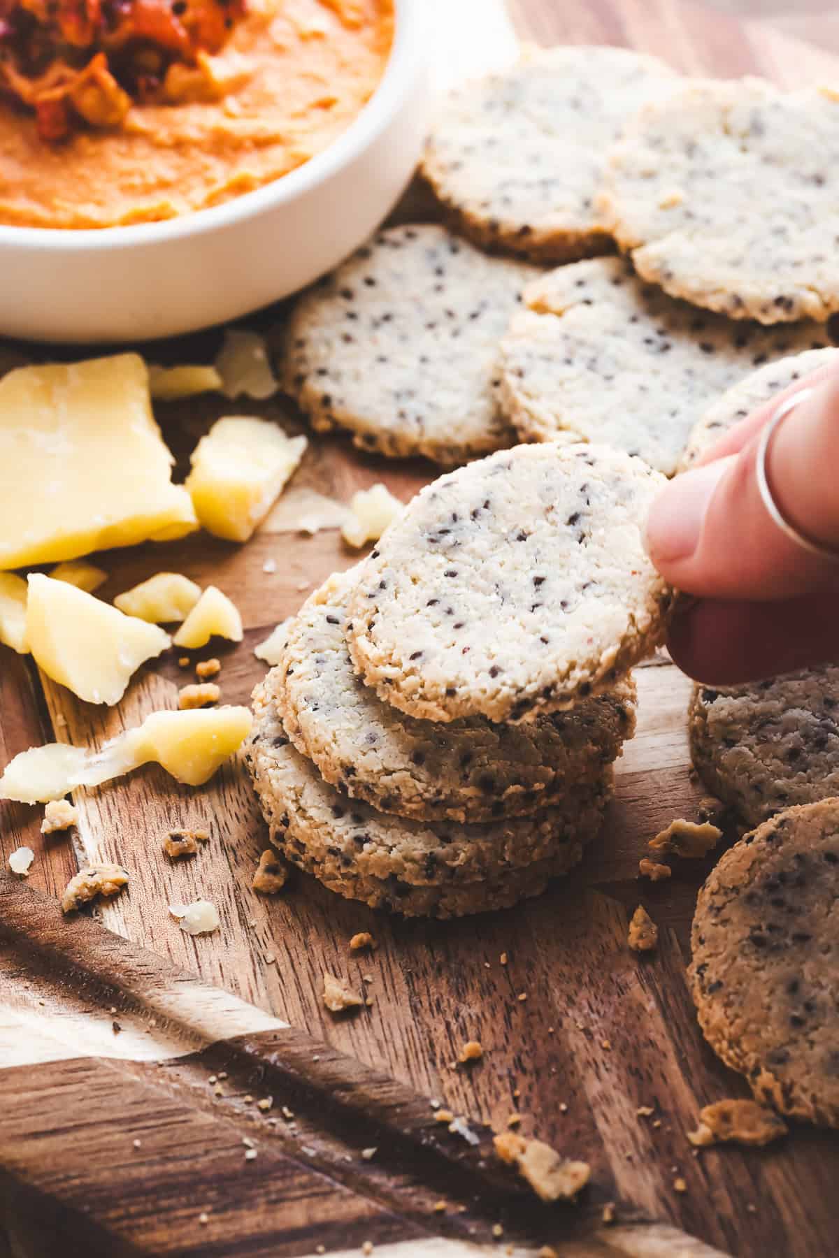 A cracker being lifted off a stack on a charcuterie board with cheese and dip.