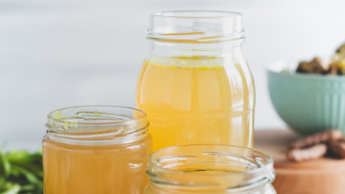 Three jars filled with golden chicken broth.