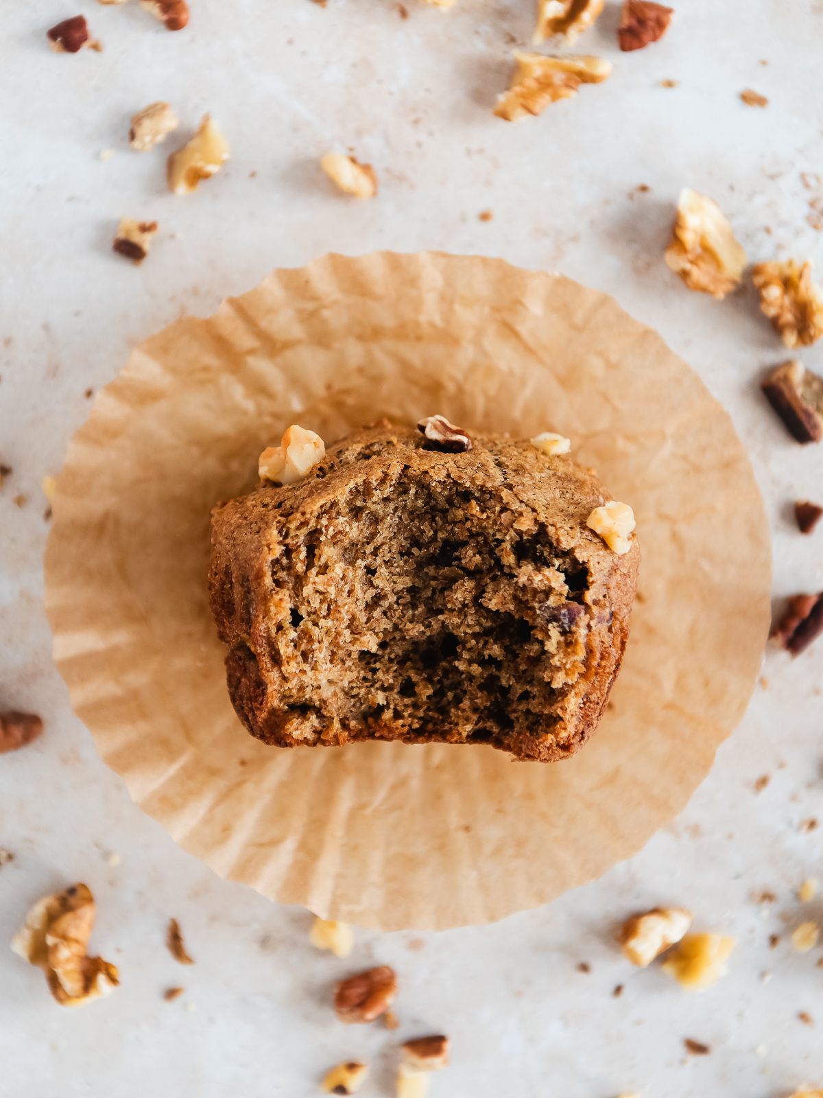 A bitten banana muffin surrounded by pecan and walnut pieces.