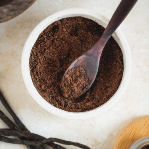 A bowl of vanilla powder beside fresh vanilla beans.