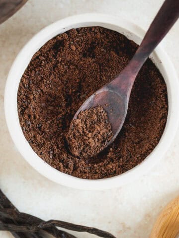 A bowl of vanilla powder beside fresh vanilla beans.