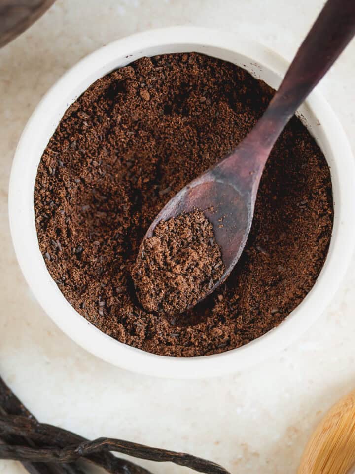 A bowl of vanilla powder beside fresh vanilla beans.