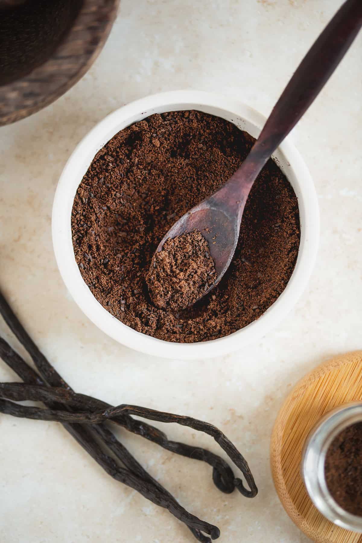 A bowl of vanilla powder beside fresh vanilla beans.