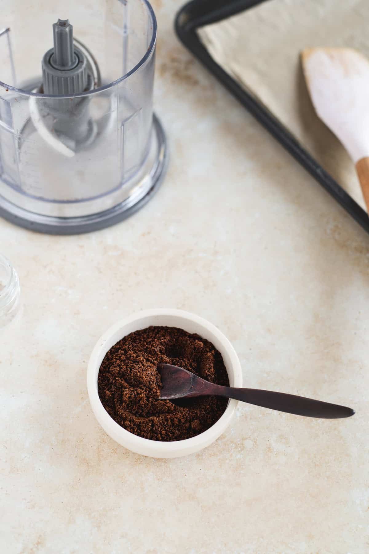 A bowl of vanilla powder beside a baking sheet and a mini food processor.
