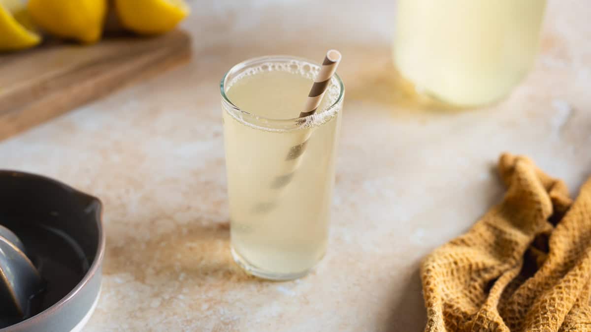 A glass of translucent yellow Lemon Soda with a gray-and-white striped straw.