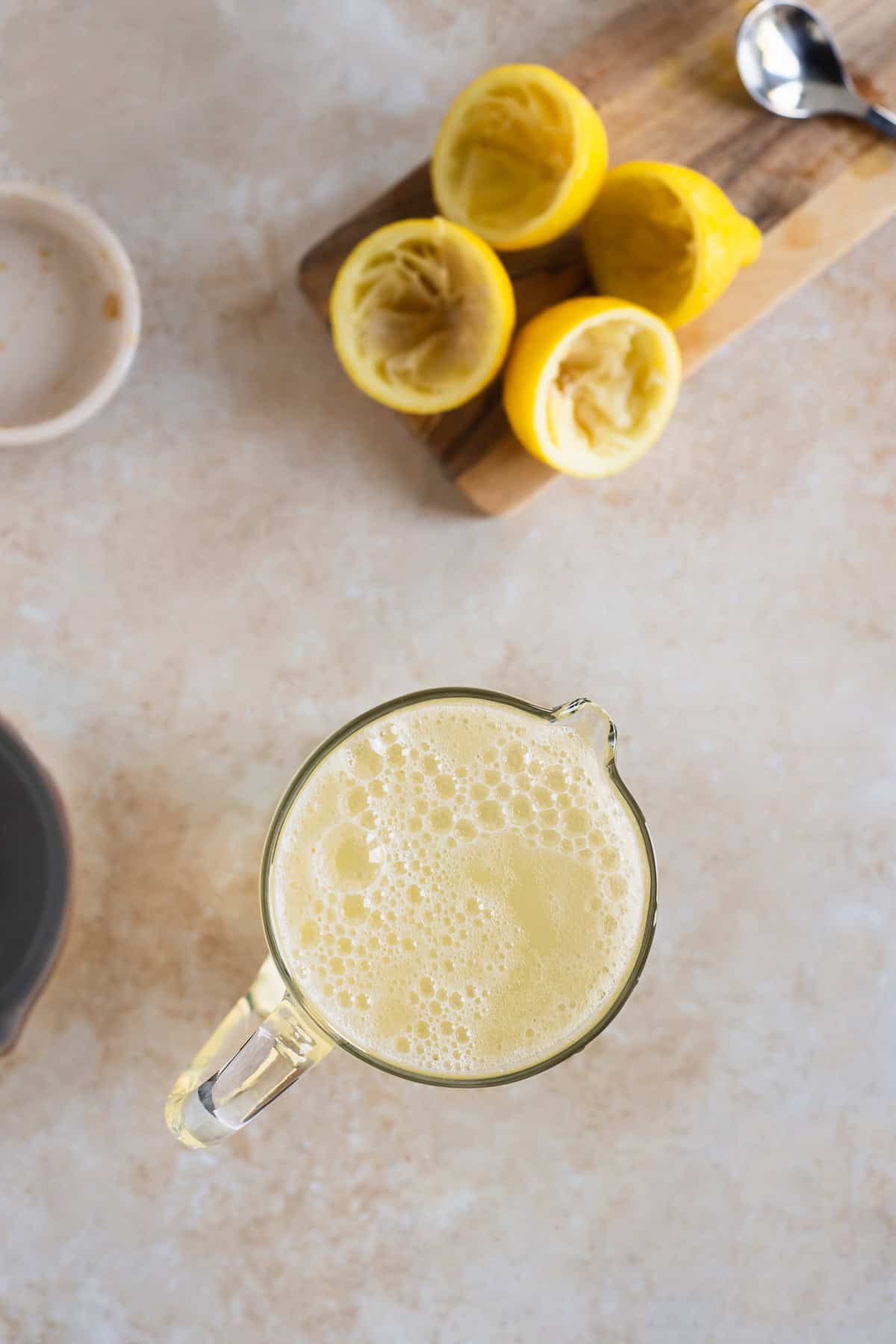 A bird's-eye view of bubbly lemon soda freshly poured into a glass pitcher beside a cluster of juiced lemon halves.