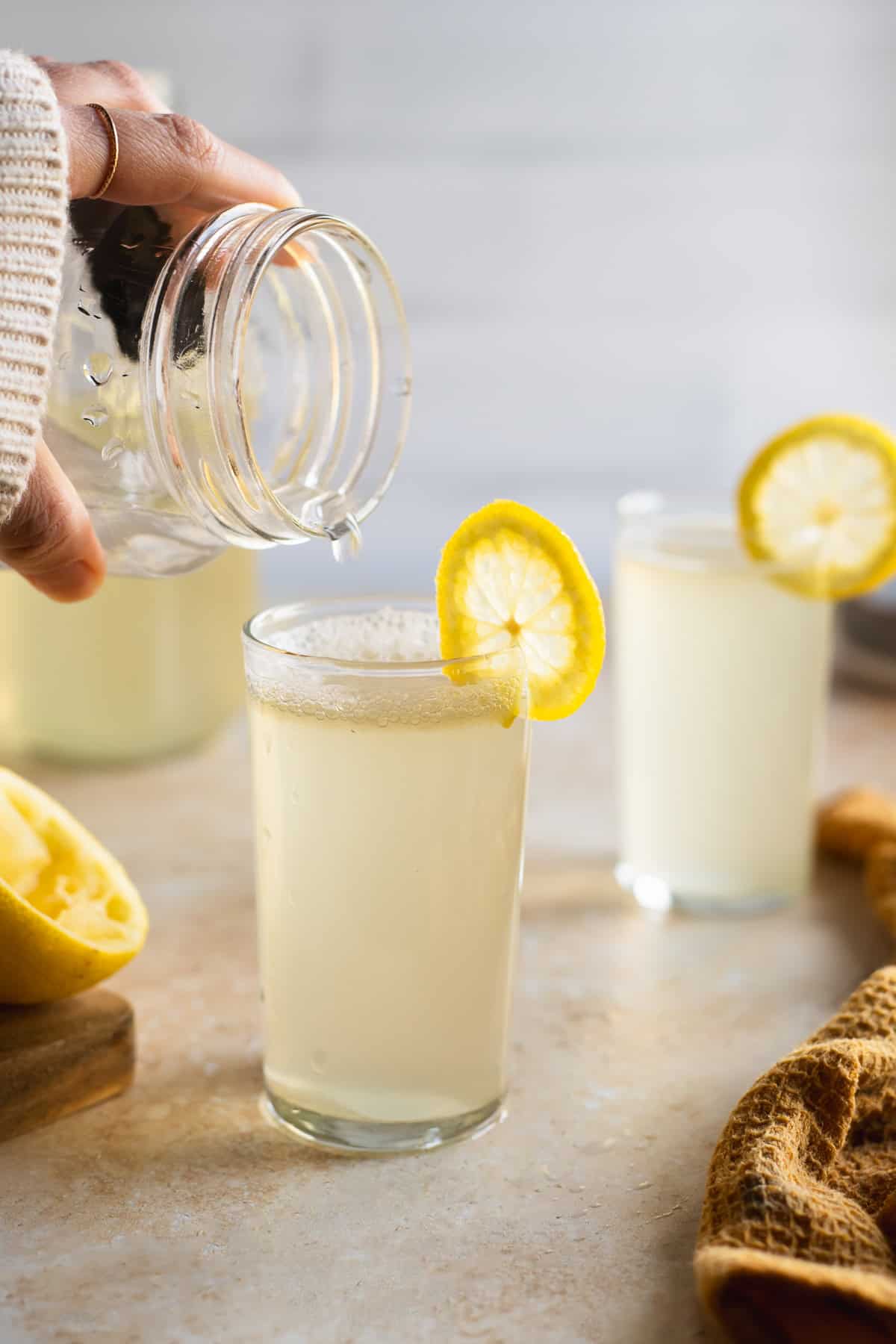 A drop of soda falling from a jug into a full glass garnished with lemon.