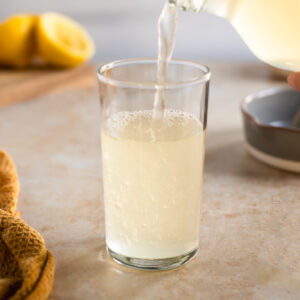 Fizzy homemade lemon soda pouring into a drinking glass.