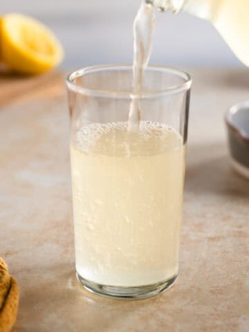 Fizzy homemade lemon soda pouring into a drinking glass.