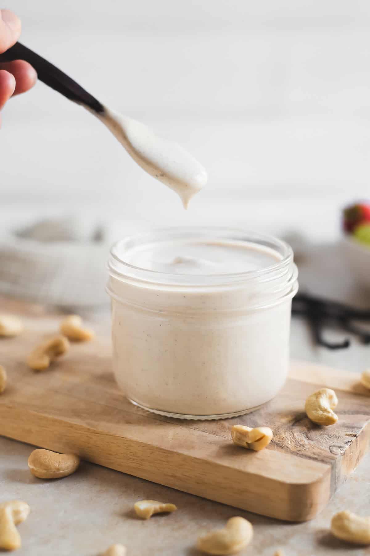 A spoonful of vanilla specked sweet cashew crème lifting out of a glass jar.