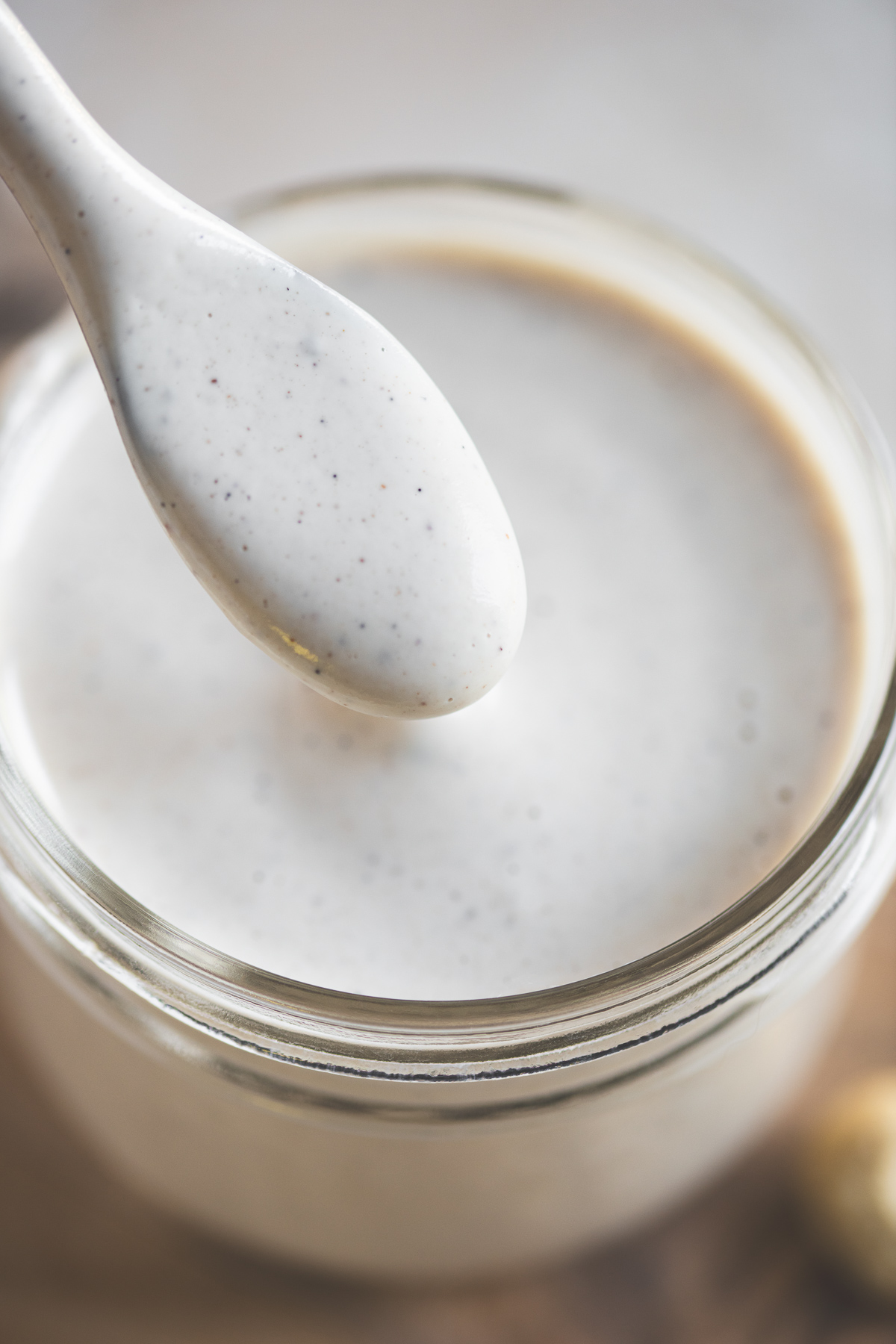 A close up of a spoon lifting vanilla speckled sweet cream from a glass jar, showcasing its smooth, creamy texture.