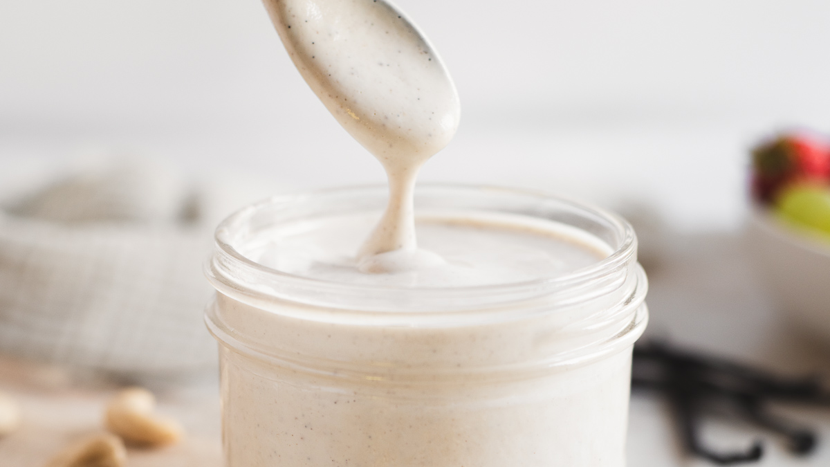 Thick, creamy vanilla-cashew crème dripping from a spoon into a full jar.