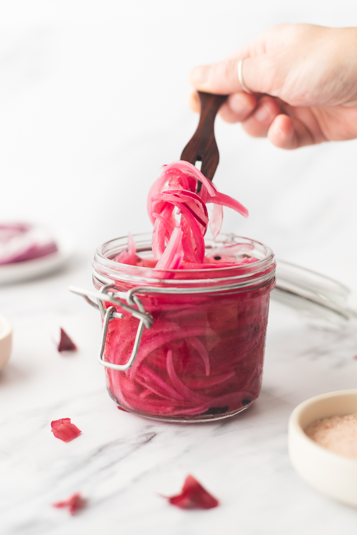 Pickled red onions being lifted from a glass jar with a wooden appetizer fork.