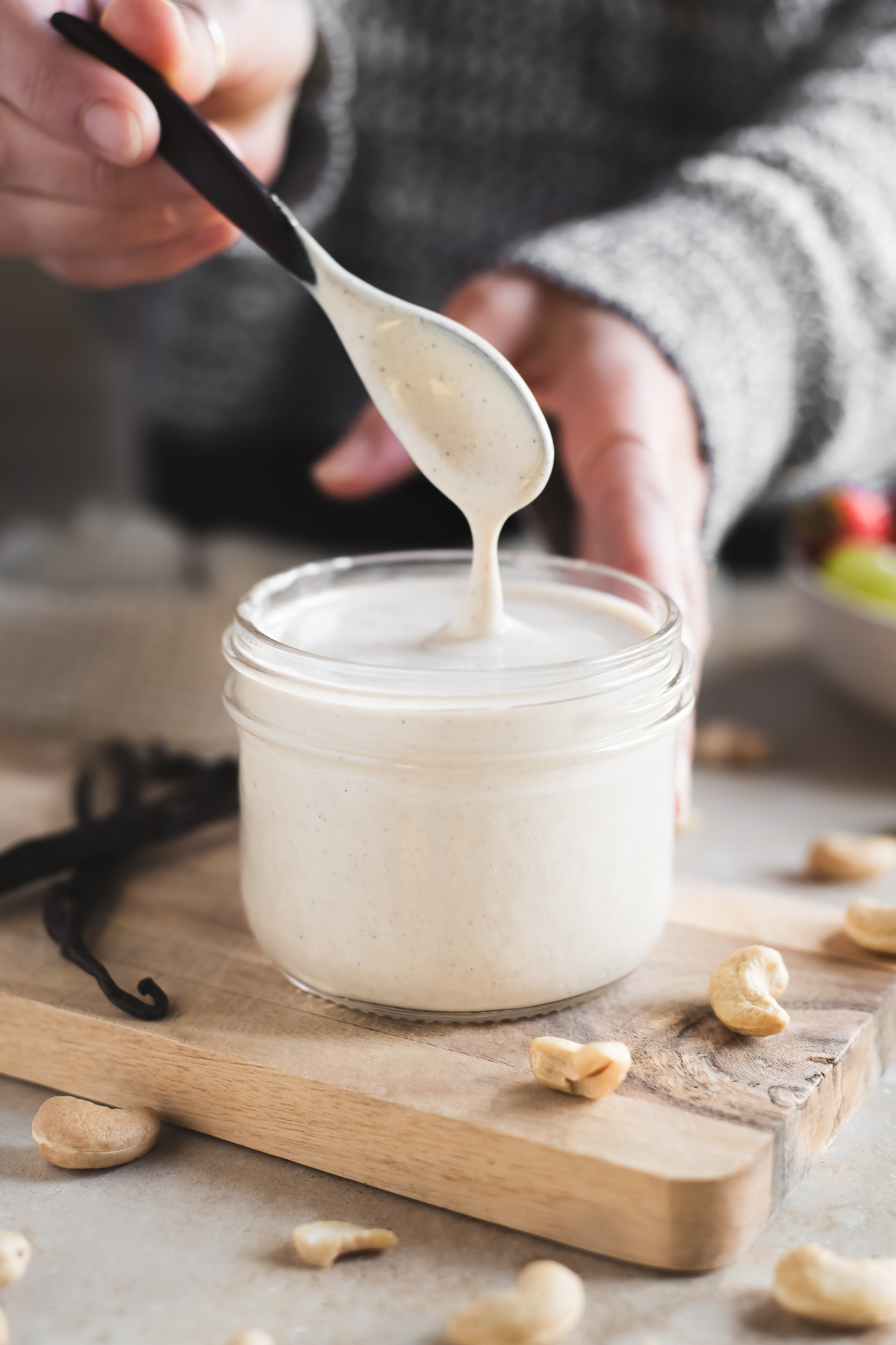A woman lifting a dripping spoon from a jar of sweet cashew crème.