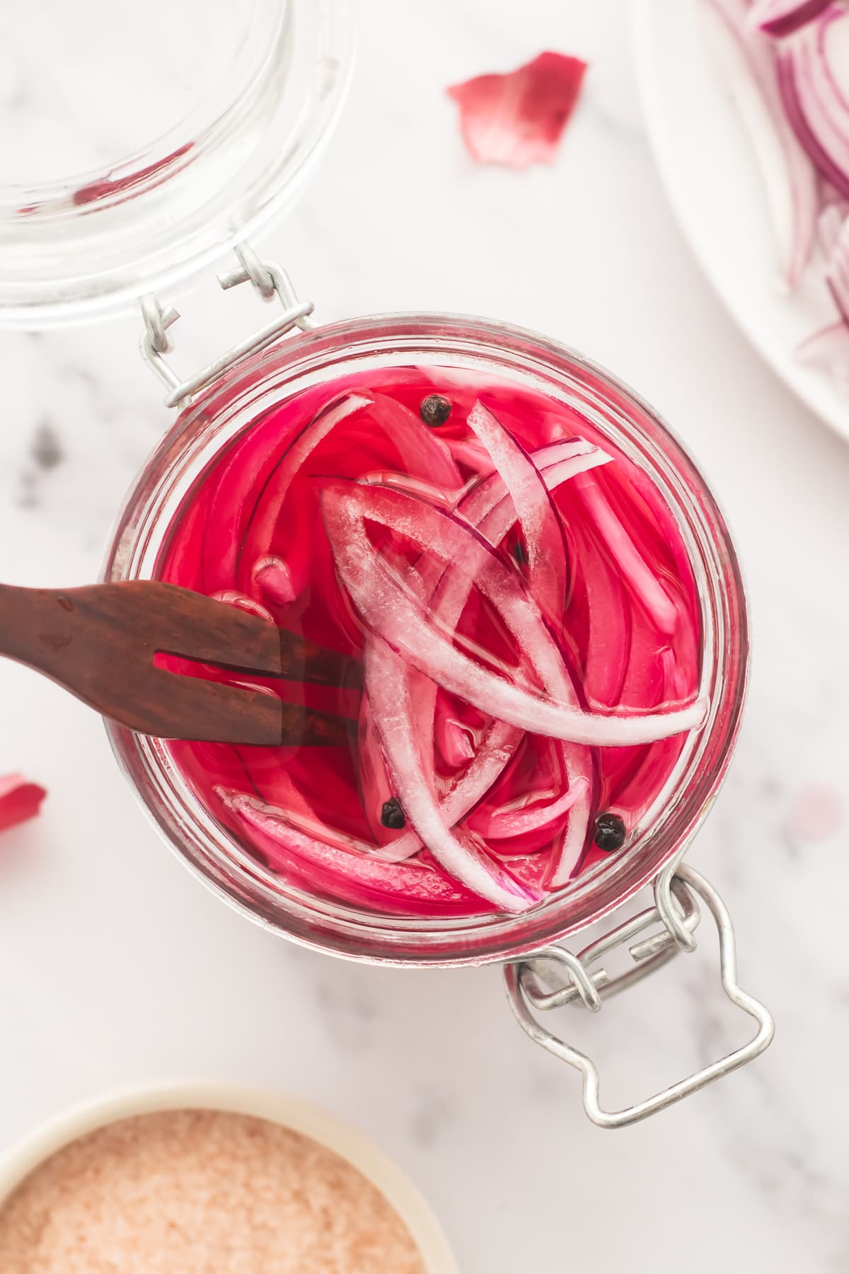 A serving fork placed in an open latch-jar filled with pickled red onions in a vibrant pink brine.