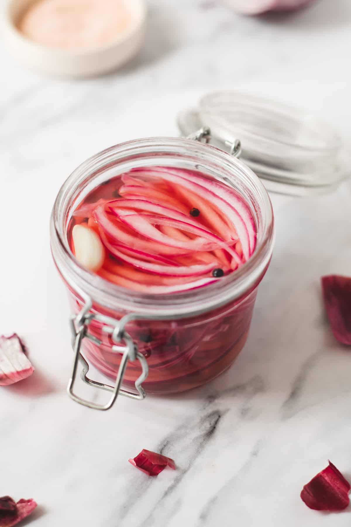 A jar of sliced red onion, peppercorns and a garlic clove covered in apple cider vinegar brine.