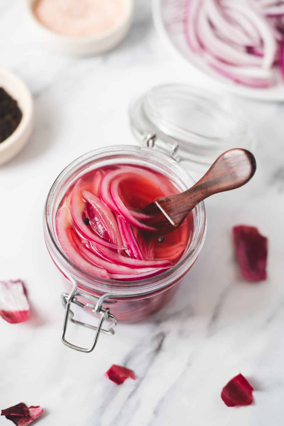 A wooden serving fork inserted in a jar of pickled red onions.