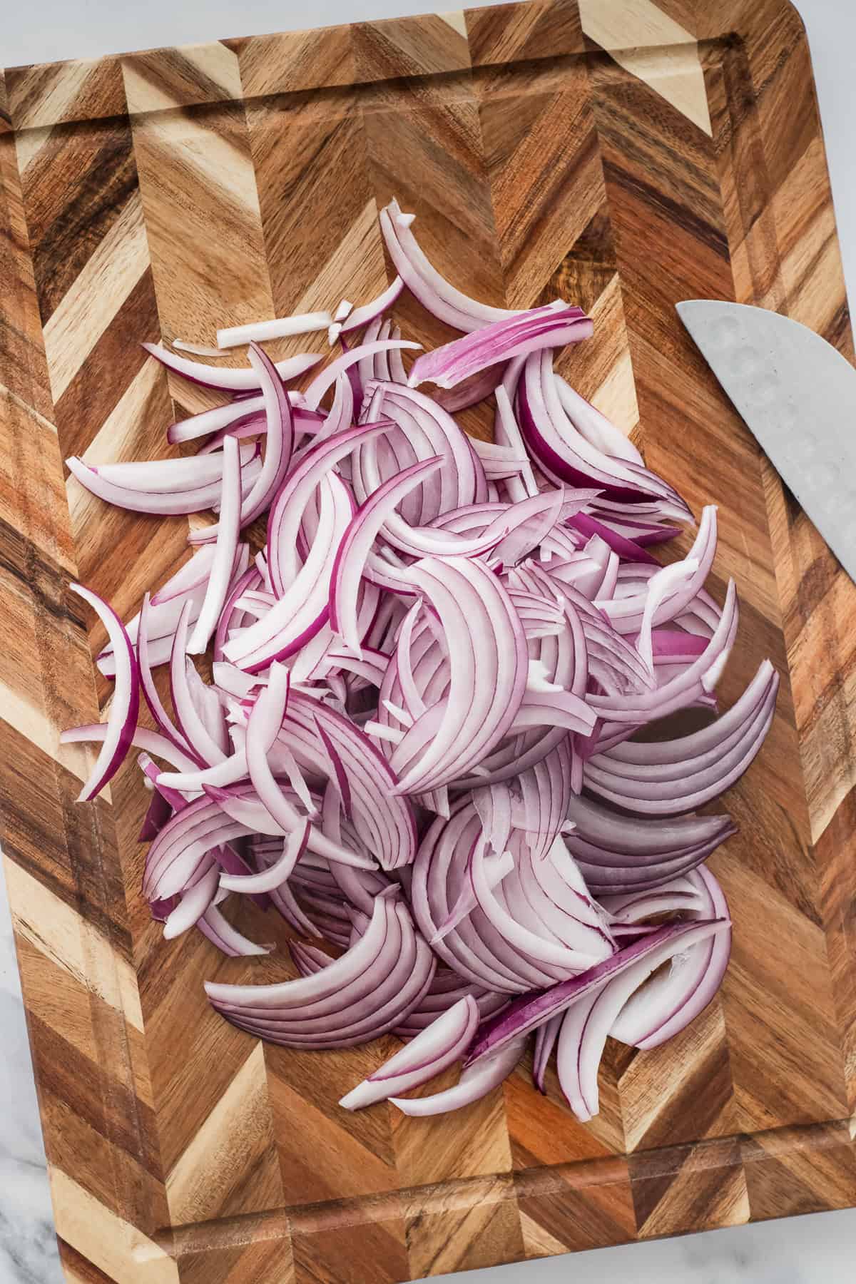 A heap of sliced red onion on a cutting board.